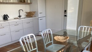 Une cuisine moderne avec des meubles blancs, un réfrigérateur blanc et une table à manger en verre entourée de chaises blanches.
