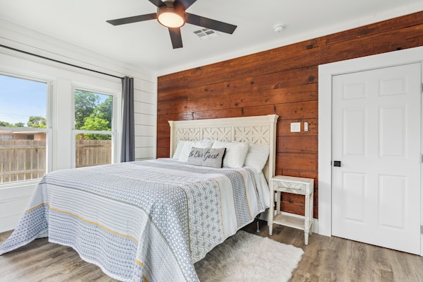 A bedroom with a bed, a nightstand, a ceiling fan, and a view of the outdoors.