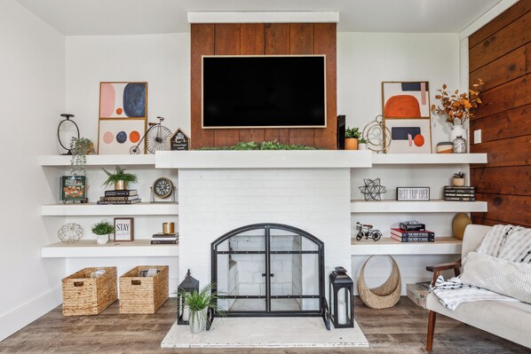 A living room with a fireplace, a mounted TV, and shelves with books and decorative items.