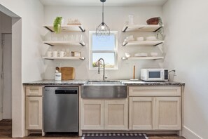 Una cocina con lavavajillas de acero inoxidable, microondas y pileta. Hay muebles blancos, una encimera de granito y una ventana sobre la pileta.
