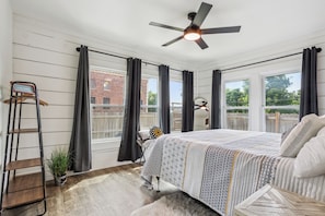A bedroom with a bed, a ceiling fan, a window with curtains, a ladder, and a small plant.