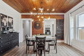 A dining area with a wooden ceiling, a chandelier, a world map on the wall, a coffee machine, and a black cabinet.
