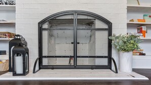 A fireplace with a metal screen, a lantern, and a potted plant. - Downtown Gem near Silos, Baylor, Cameron Park... (Waco)