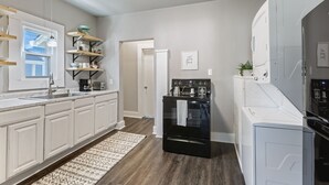 A modern kitchen with white cabinets, a black oven, and a built-in washer and dryer. - Downtown Gem near Silos, Baylor, Cameron Park... (Waco)