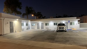 Un estacionamiento con un coche blanco, un edificio con varias puertas y ventanas, y un letrero de estacionamiento para discapacitados.