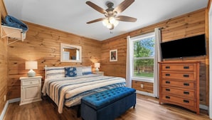 A bedroom with a bed, a ceiling fan, a dresser, a window, and a TV.