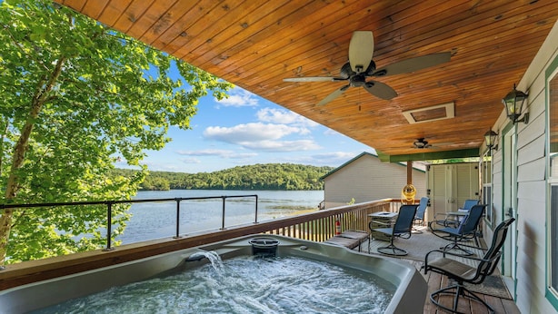 A hot tub on a wooden deck with a view of a lake and hills.
