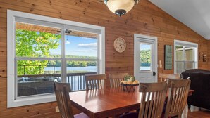 A wooden-paneled room with a dining table, chairs, a clock, and a view of a lake.