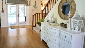 Una habitación amplia con piso de madera, un tocador blanco, un espejo redondo y una escalera que conduce a otro nivel.
