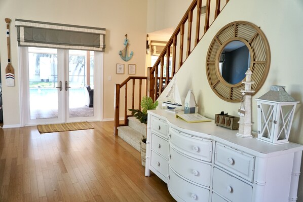 A spacious room with hardwood flooring, a white dresser, a round mirror, and a staircase leading to another level.