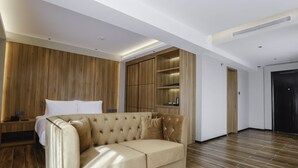 A modern hotel room with a beige sofa, wooden panel walls, and a built-in wardrobe. - Hotel Casiana and Events Center Tagaytay (Tagaytay)