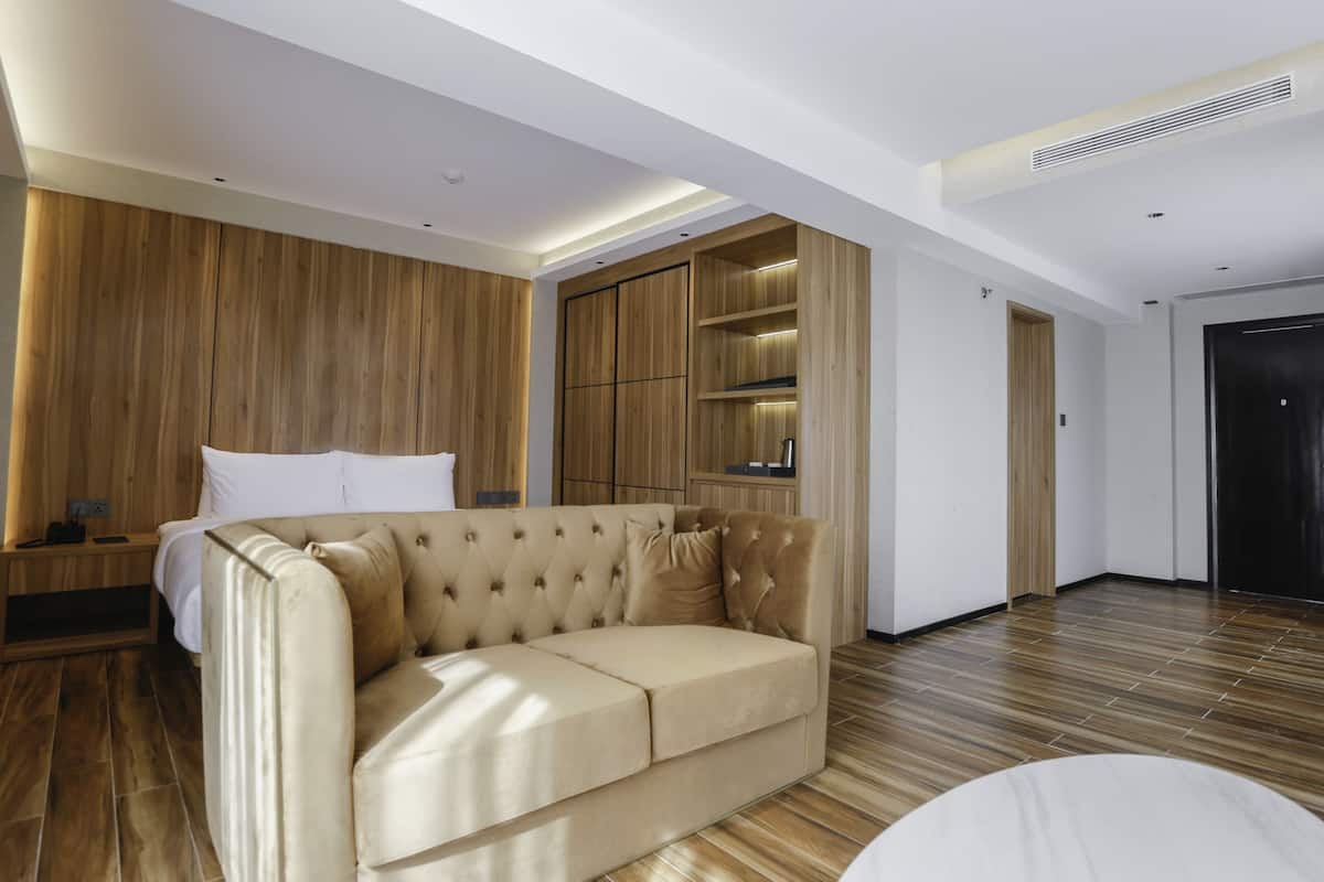 A modern hotel room with a beige sofa, wooden panel walls, and a built-in wardrobe.