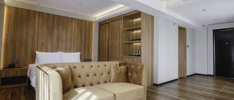 Ein modernes Hotelzimmer mit einem beigefarbenen Sofa, Holzwandverkleidung und einem integrierten Kleiderschrank.