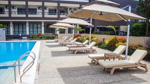 A poolside area with lounge chairs and umbrellas, a pool, and a building in the background. - Hotel Casiana and Events Center Tagaytay (Tagaytay)
