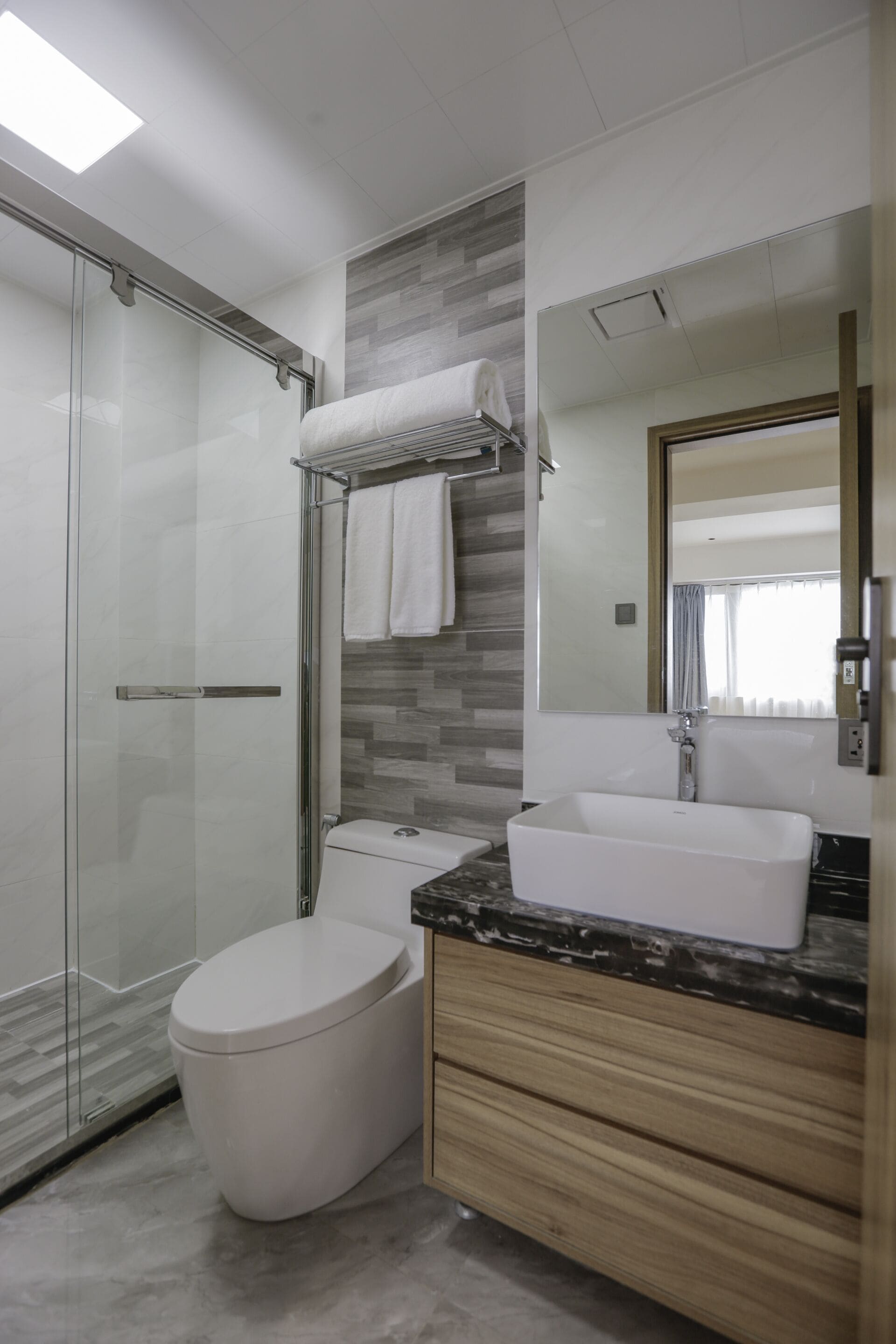 A modern bathroom with a glass-enclosed shower, a white toilet, a vanity with a large sink, and a mirror.