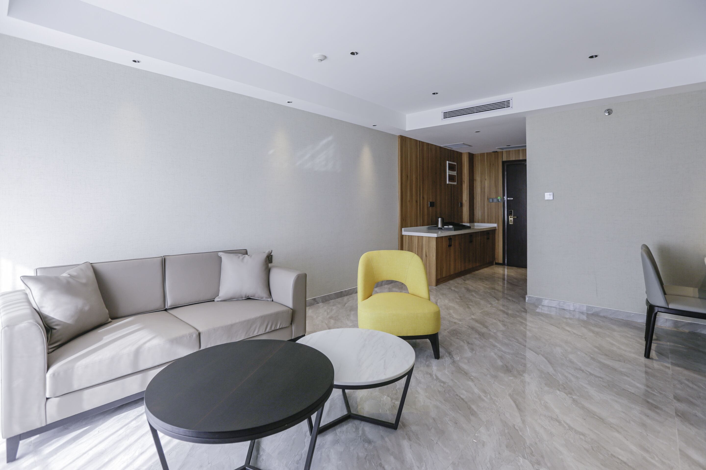 A modern living room with a sofa, two chairs, a coffee table, and a kitchen area in the background.