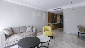 A modern living room with a sofa, two chairs, a coffee table, and a kitchen area in the background.