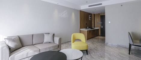 A modern living room with a sofa, two chairs, a coffee table, and a kitchen area in the background.