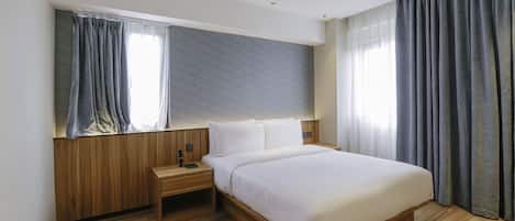 A modern hotel room with a wooden headboard, a large bed, a nightstand, and a window with curtains.