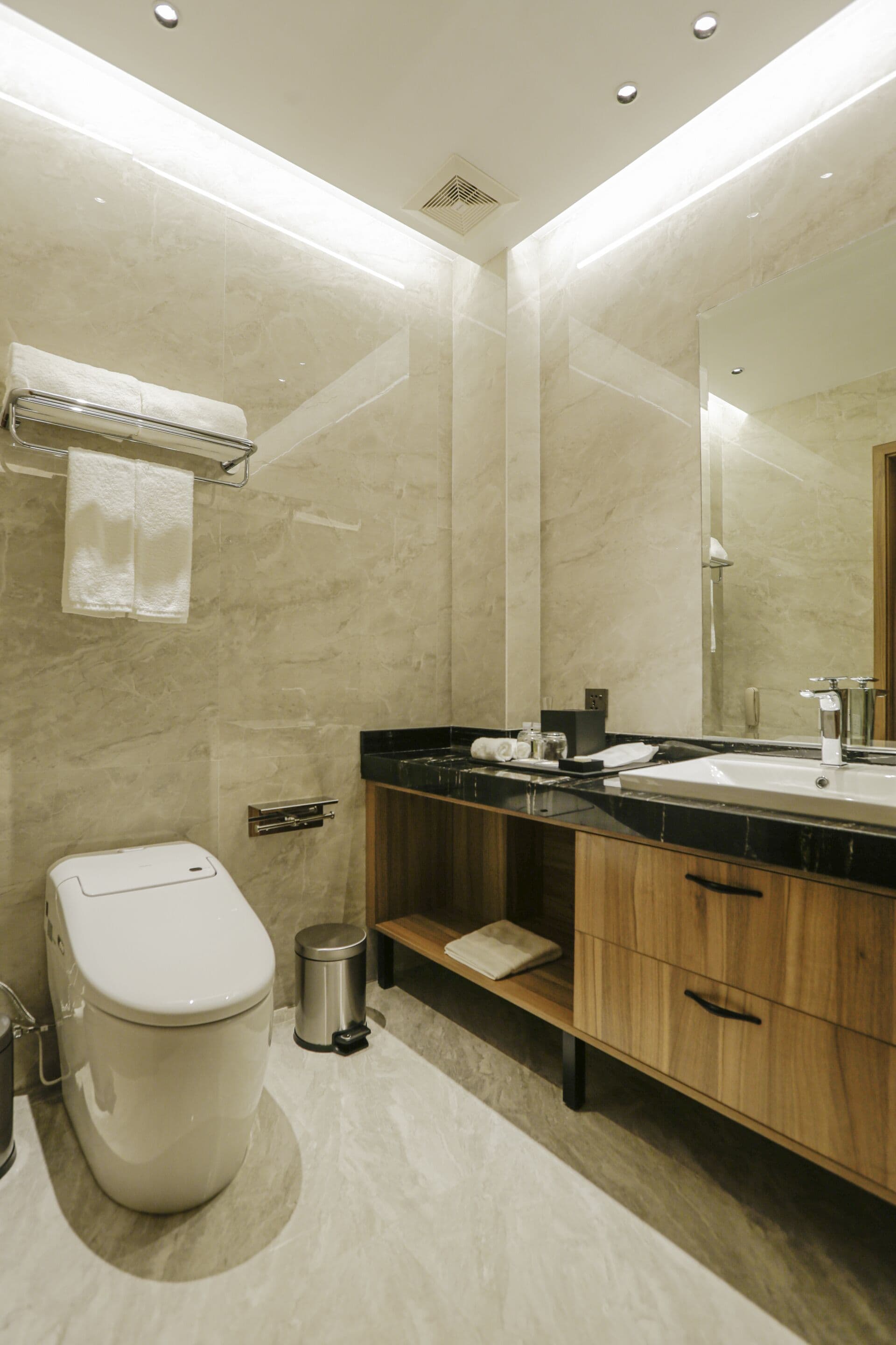 A modern bathroom with a toilet, sink, mirror, and wooden cabinet.