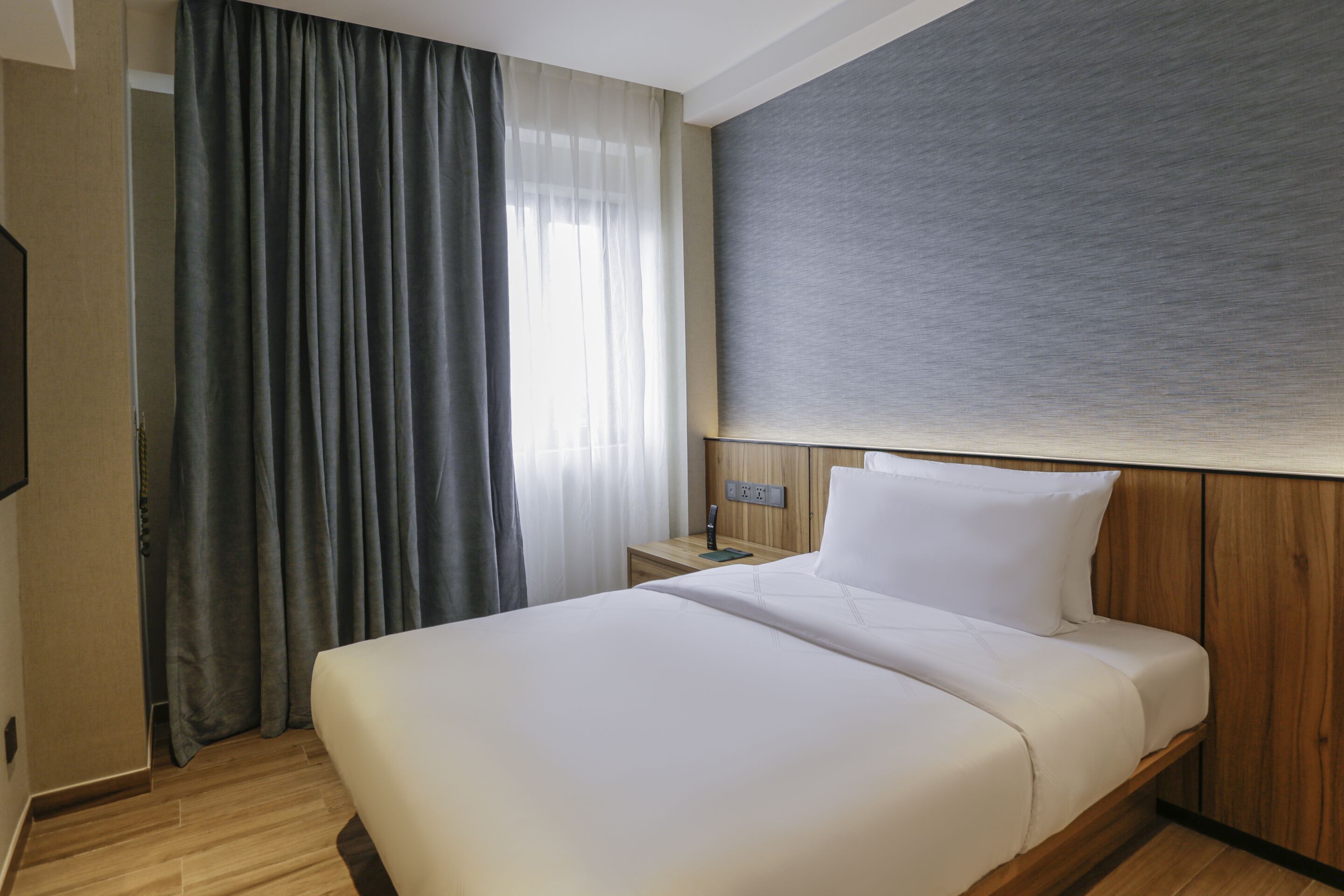 A hotel room with a large bed, wooden headboard, a nightstand, and a wall-mounted TV.