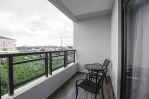 Ein Balkon mit Tisch und Stühlen, Blick auf Grünflächen und Gebäude, sowie eine Glastür.