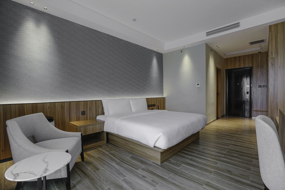 A modern hotel room with a large bed, a bedside table, a chair, and a small table.