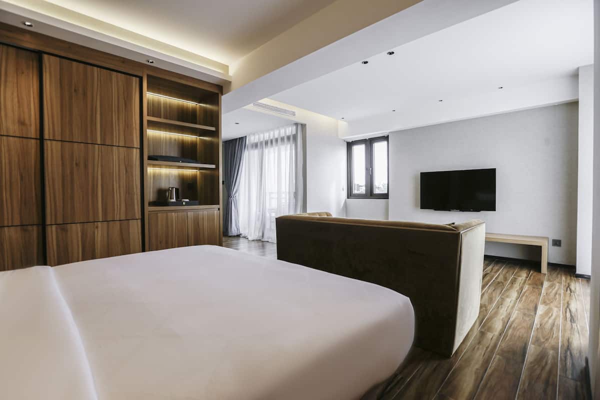 A modern hotel room with a large bed, wooden wardrobe, a flat-screen TV, and a seating area.