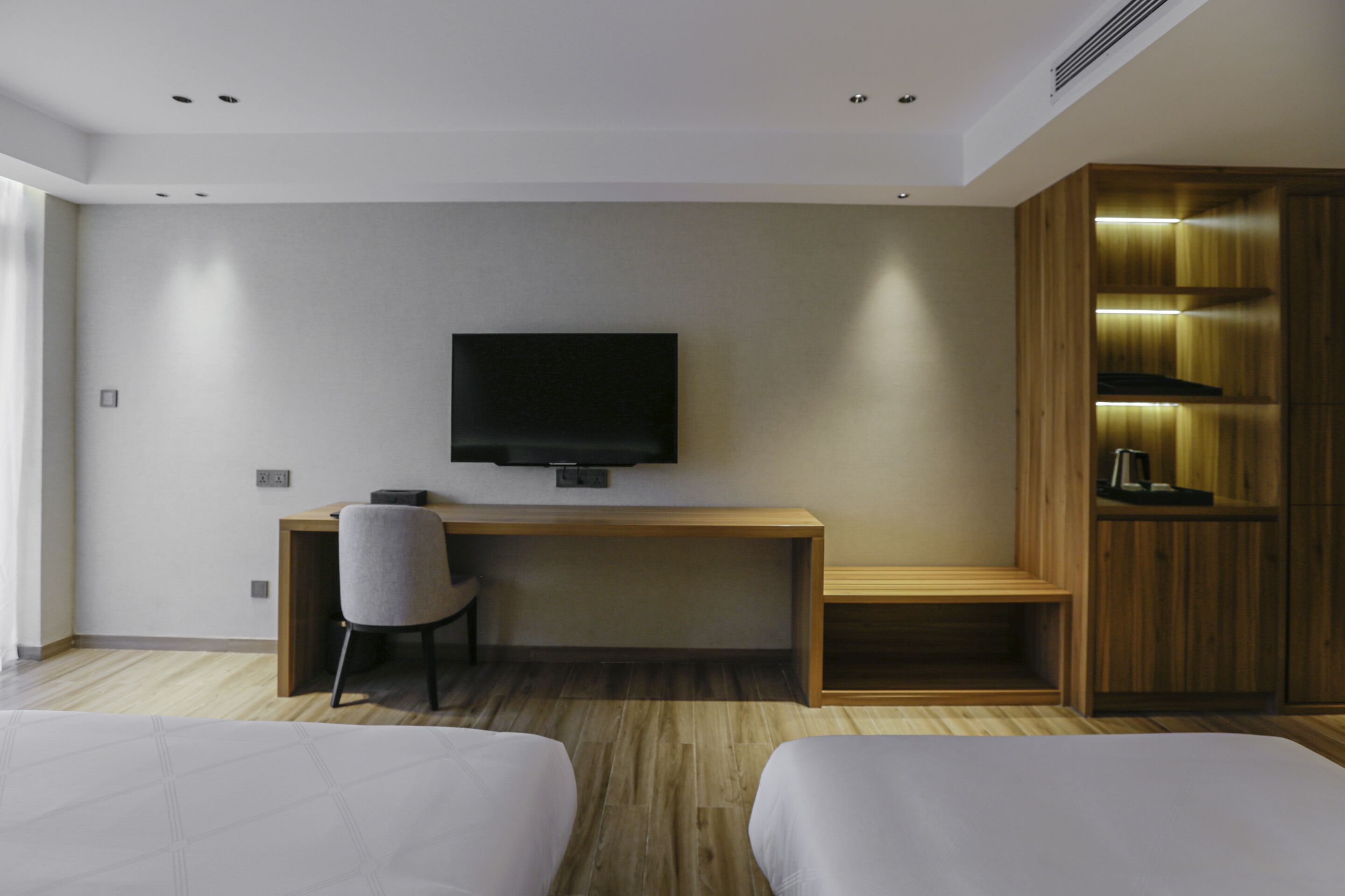 A modern hotel room with a wooden desk, a flat-screen TV, a chair, and two beds.
