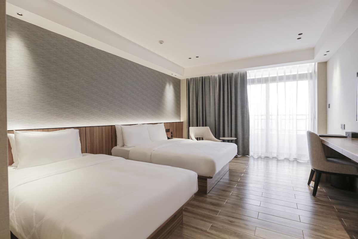 A hotel room with two beds, a desk, and a chair.