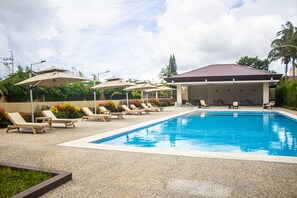 Ein Swimmingpool mit Liegestühlen und Sonnenschirmen, umgeben von einem Gebäude mit rotem Dach.