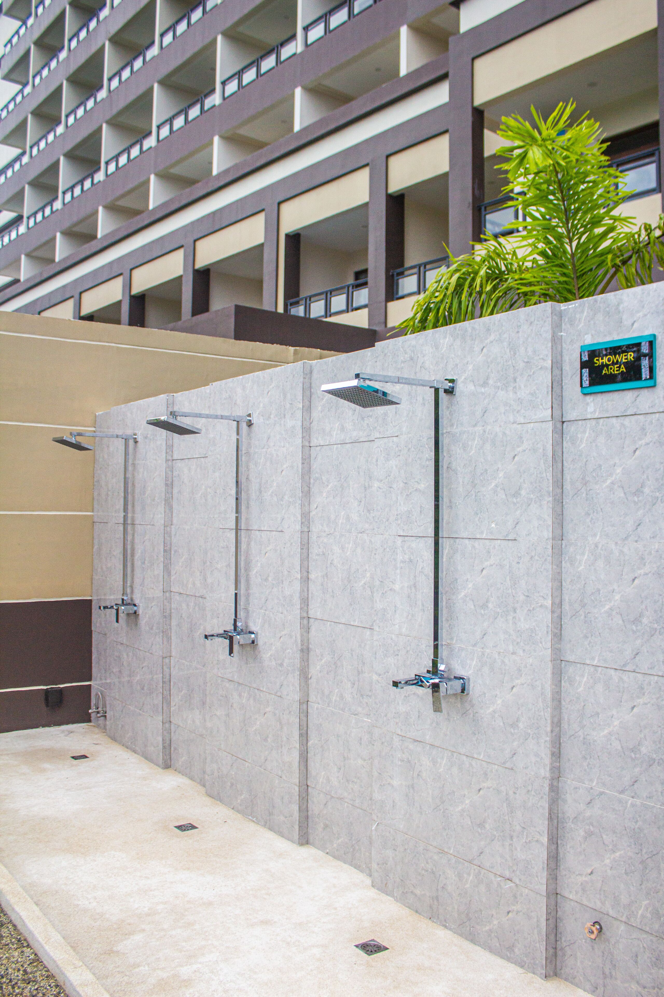 A row of shower cubicles with a sign indicating a shower area, set against a building with multiple floors and balconies.