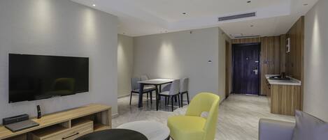 Una sala moderna con un televisor de pantalla plana, una mesa de centro redonda, un sillón amarillo, un sofá gris y un comedor con mesa y sillas.
