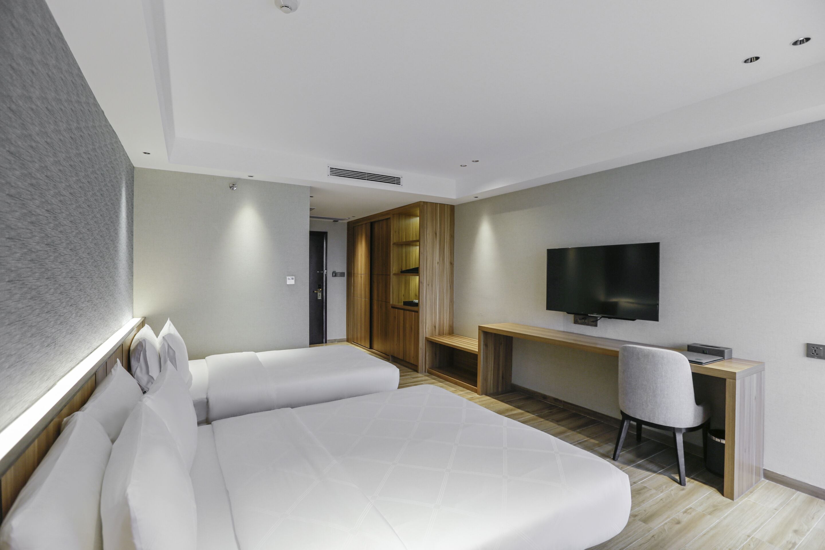 A modern hotel room with a large bed, a desk, a chair, and a flat-screen TV.