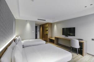 A modern hotel room with a large bed, a desk, a chair, and a flat-screen TV.