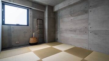 A room with tatami mats, a concrete wall, a window, and a hanging rack with clothes.