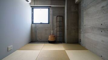 A room with tatami mats, a concrete wall, a window, and a hanging rack.