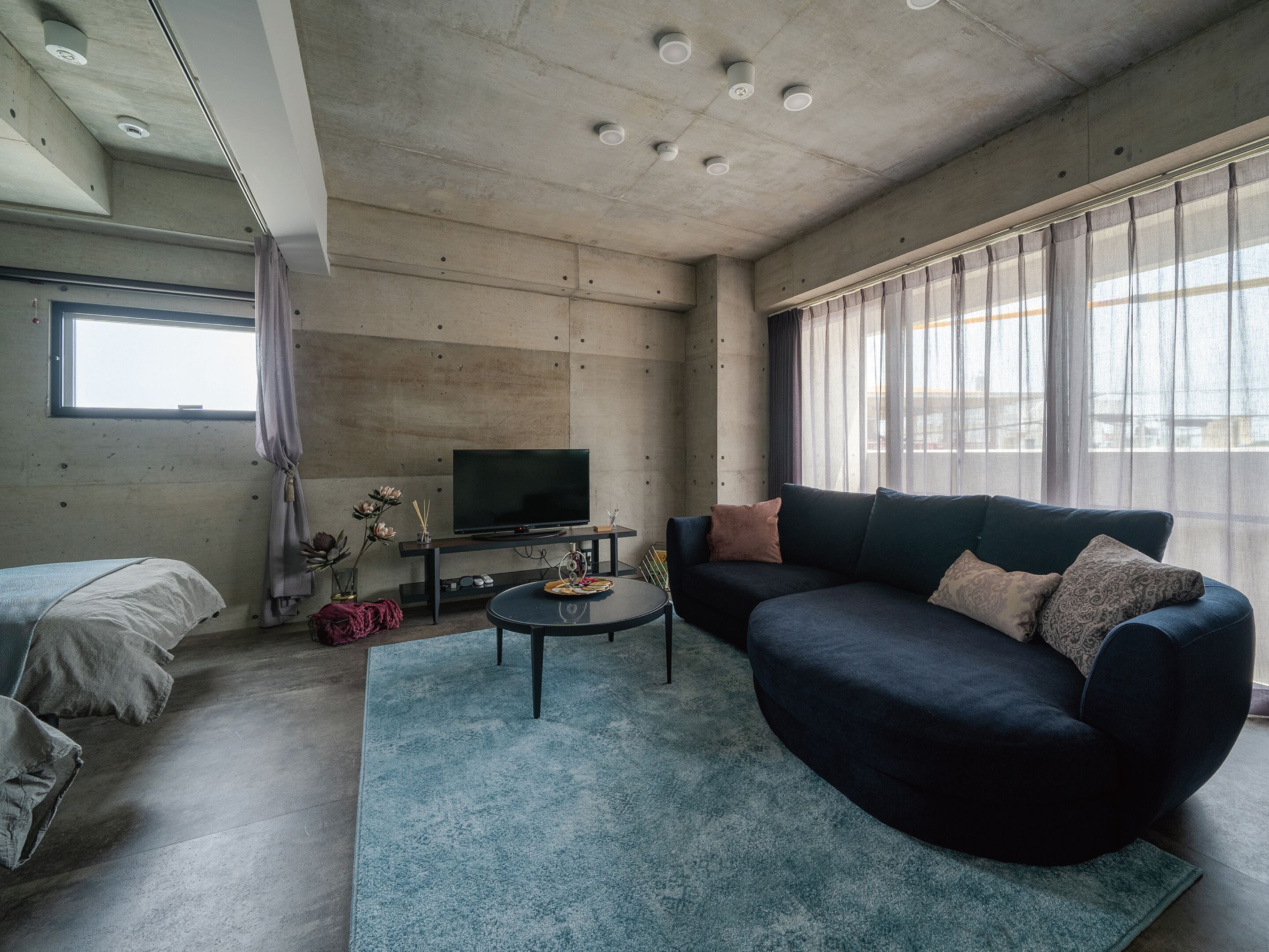 A modern living room with a sofa, a coffee table, a TV, and a large window with curtains.