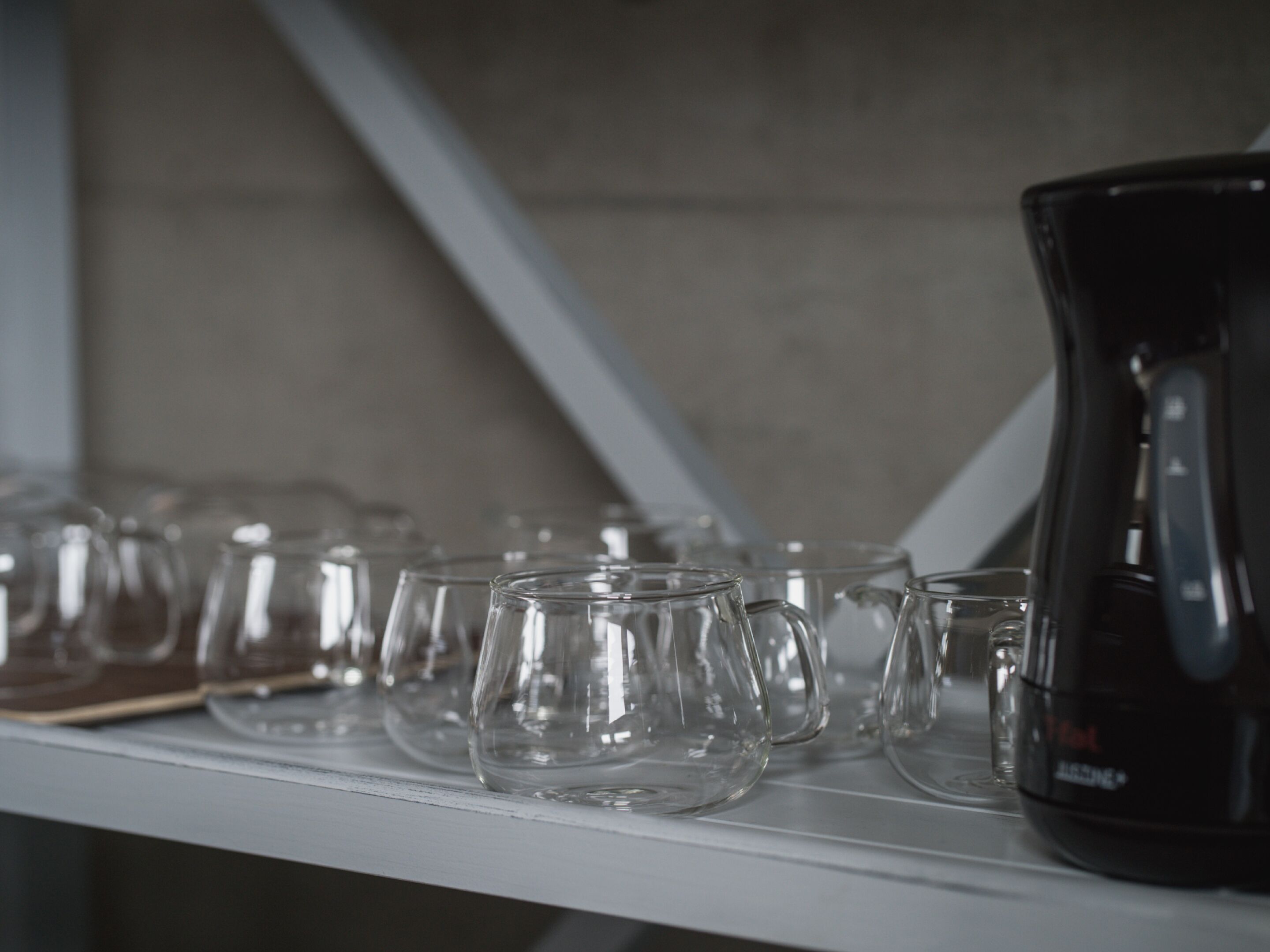 A row of empty glasses on a shelf, with a black pitcher on the right.
