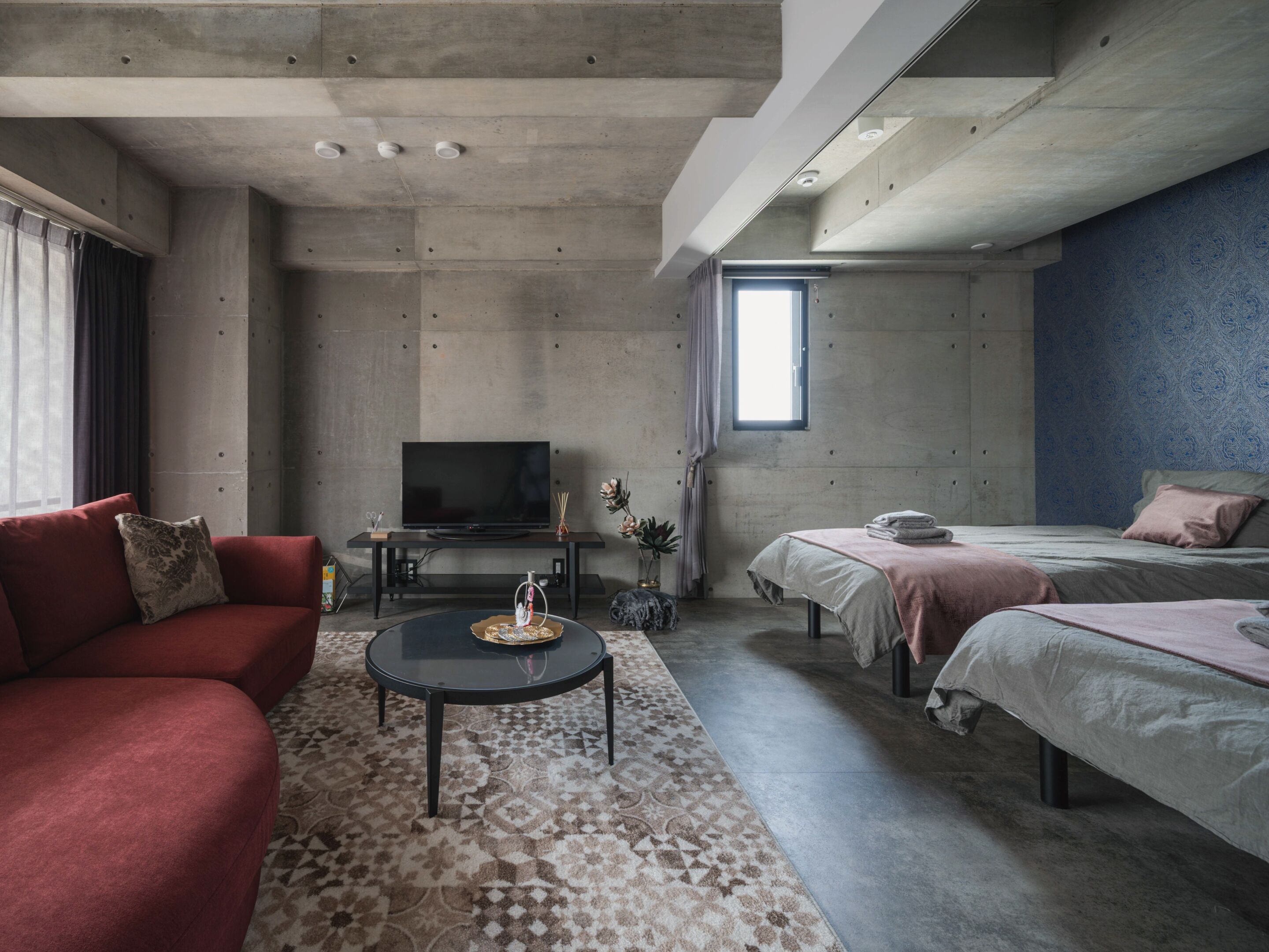 A modern living room with a sofa, a coffee table, a TV, and a bed with a headboard.