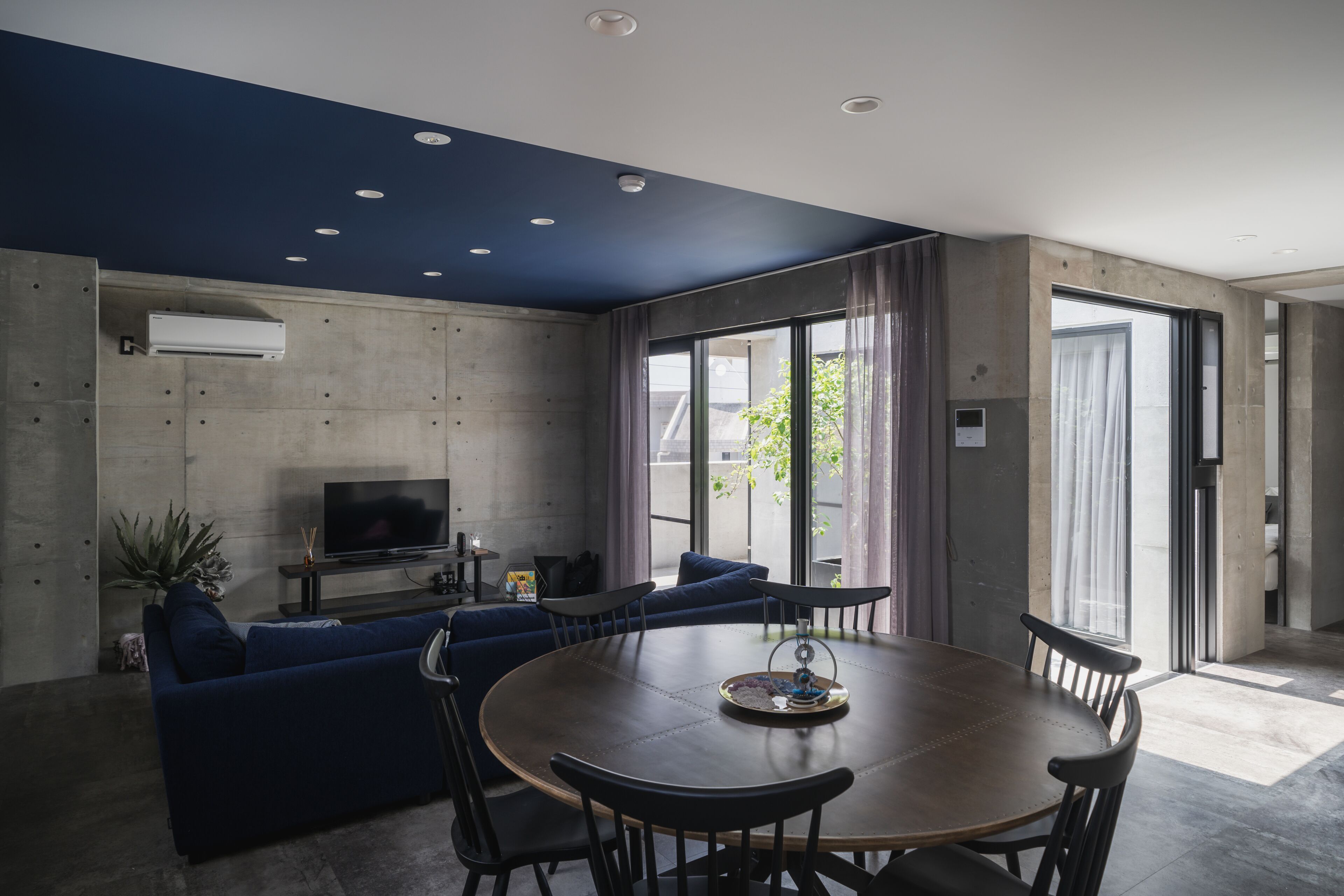 A modern living room with a blue sofa, a wooden dining table, and a flat-screen TV.