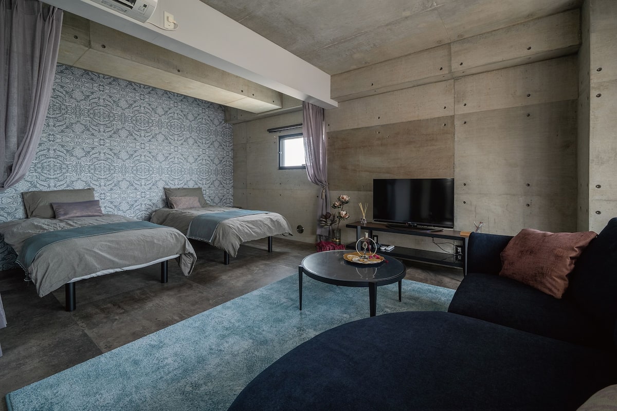 Habitación de hotel moderna con dos camas, un sofá, un televisor y una pequeña mesa.