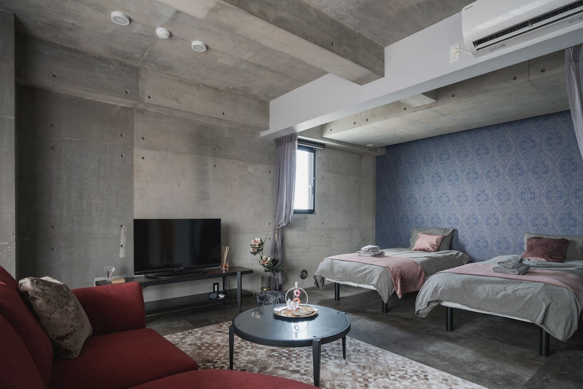 Un dormitorio moderno con sofá, dos camas, televisor y ventilador de techo.
