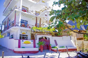 Stunning multi-story building with balconies and windows, adorned with palm tree and sun motifs, surrounded by lush greenery.