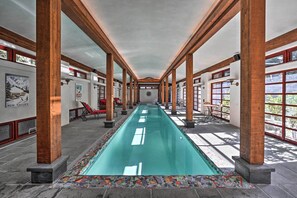 Una piscina interior larga con vigas de madera y ventanas amplias.