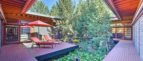 A wooden deck with red lounge chairs, a small table, and a red umbrella.