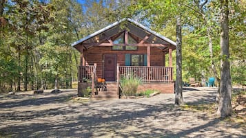 Situated in a wooded area, this cabin features a pitched roof, front porch, and a door with a decorative design.