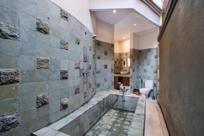 Un baño con paredes de piedra, una bañera, un inodoro y un lavamanos.