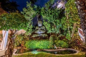 Un jardín tranquilo con una estatua de Buda, abundante vegetación y un pequeño estanque.