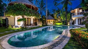 A resort with a swimming pool, thatched-roof structures, and lush greenery.